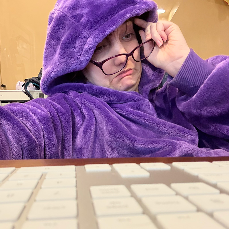 female-shaped creature in purple robe sits anguished at the computer